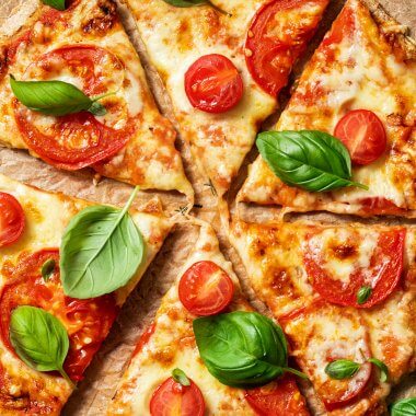 Gesunde Pizza mit einem leckeren Vollkorn Pizzateig belegt mit Tomaten, Käse und frischem Basilikum in Stücke geschnitten auf einem Backpapier.